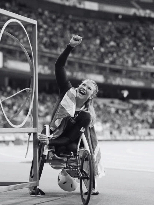 Athlete in a wheelchair raising fist in celebration at a stadium.
