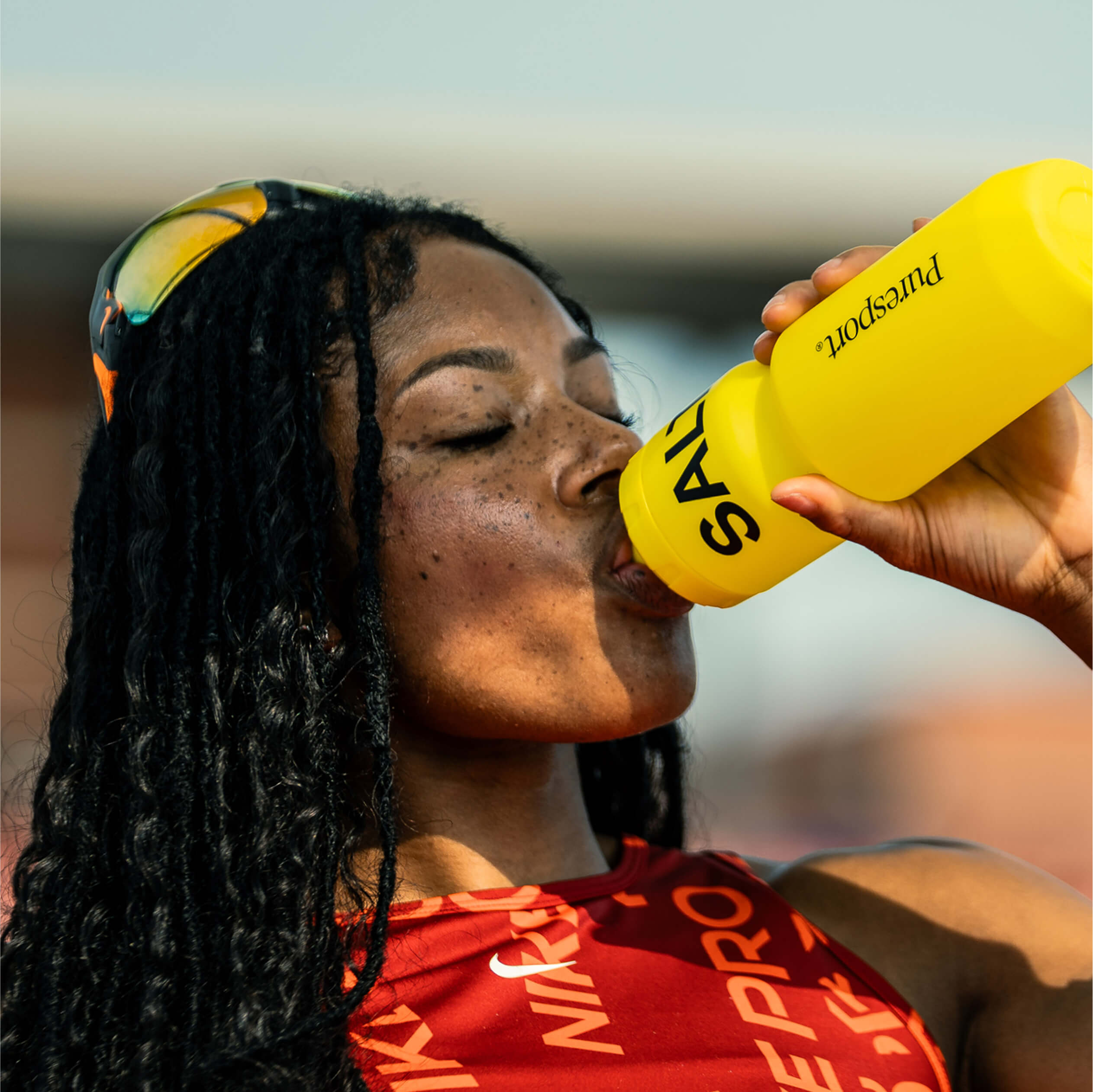 Person drinking from a yellow sports bottle outdoors.
