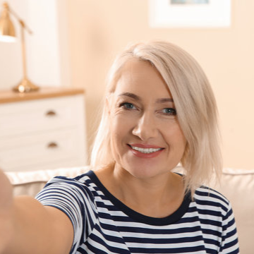 Person with short blonde hair smiling indoors, wearing a striped shirt.