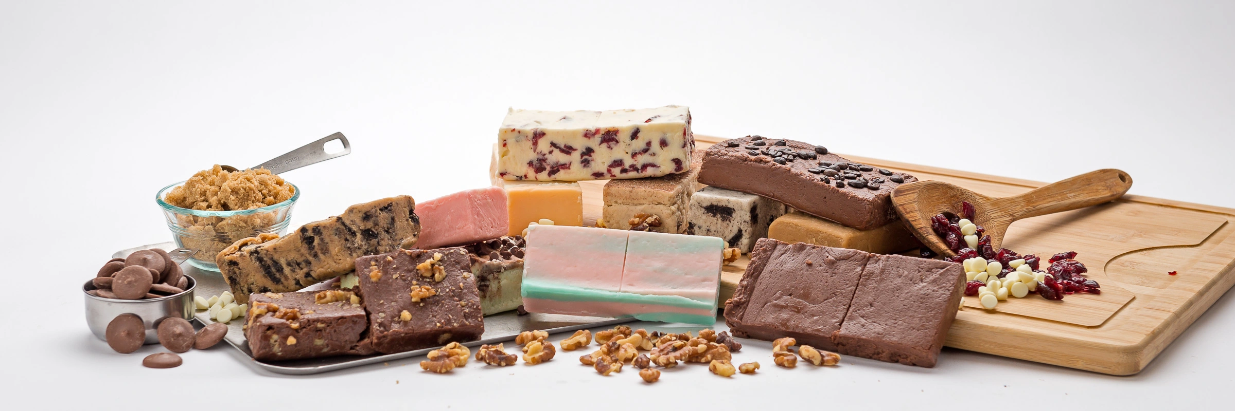 Assorted fudge pieces with nuts, chocolate, and dried fruits on a wooden board.
