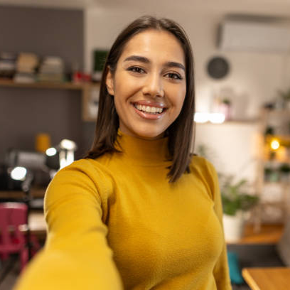Person in a yellow sweater taking a selfie in a cozy room.