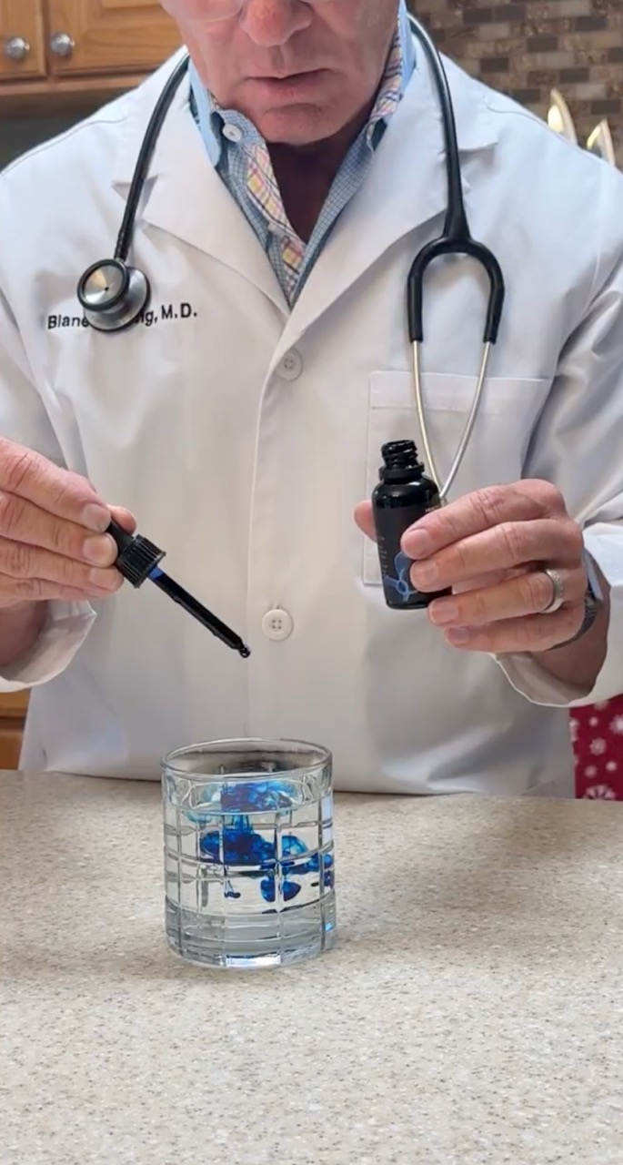 Doctor using dropper with blue liquid in a glass of water.