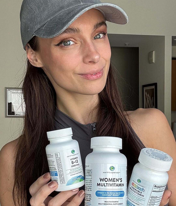 Person holding bottles of vitamins, wearing a gray cap indoors.