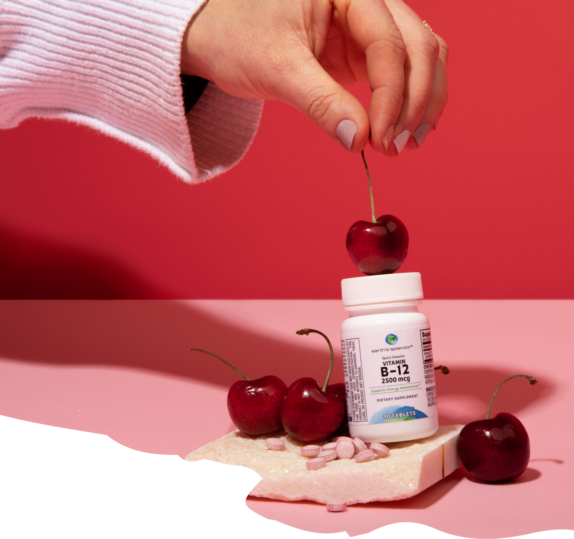 A hand holds a cherry over a bottle of Vitamin B-12 tablets, surrounded by other cherries.