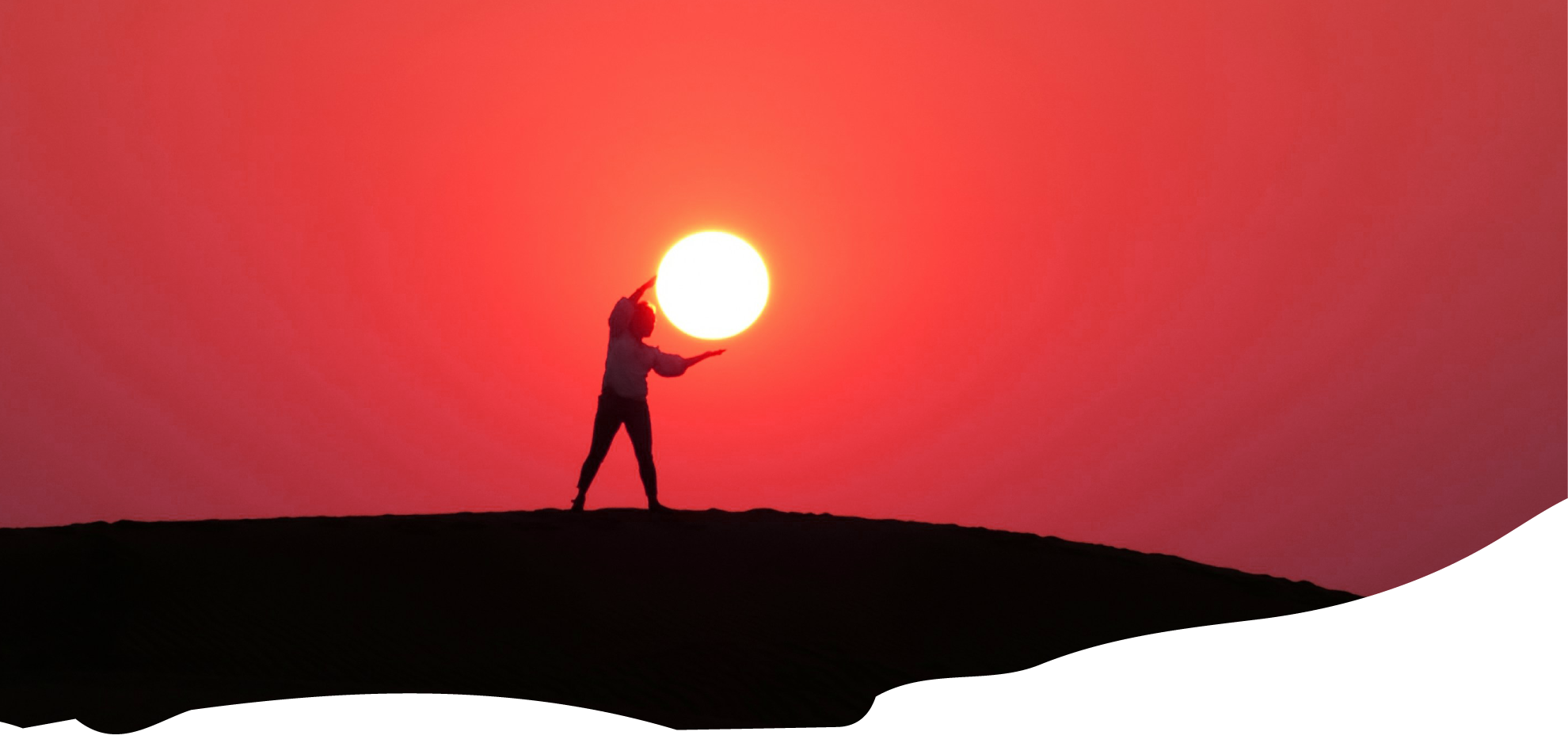 Silhouette of a person on a hill appearing to hold the sun against a vivid red sky.