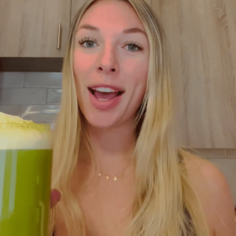 Person holding a green beverage in a kitchen setting.
