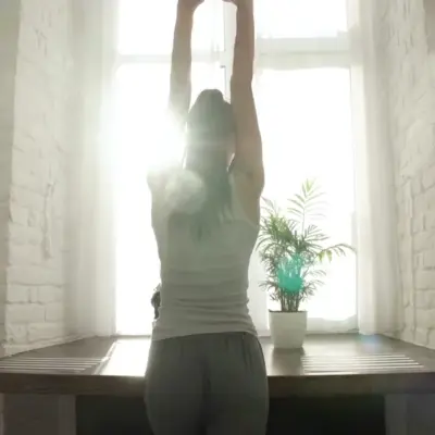 Person stretching by a window with sunlight and a potted plant.