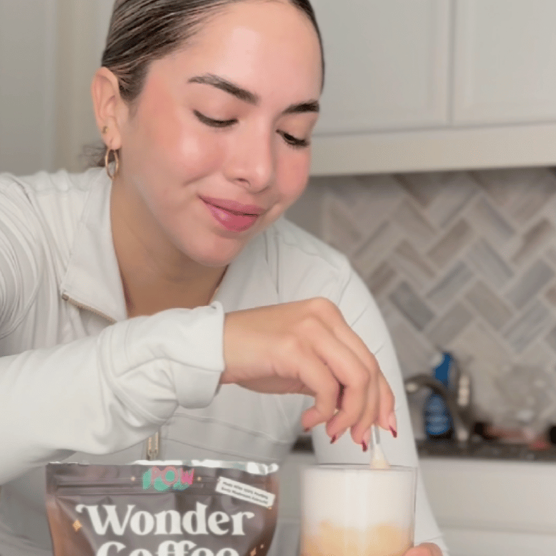 Person stirring a glass of coffee with a packet labeled 'Wonder Coffee' in the foreground.