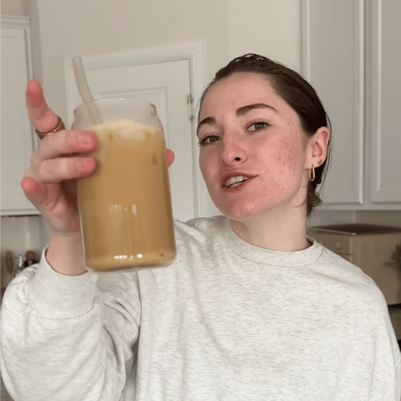 Person holding a glass of iced coffee with a straw in a kitchen.