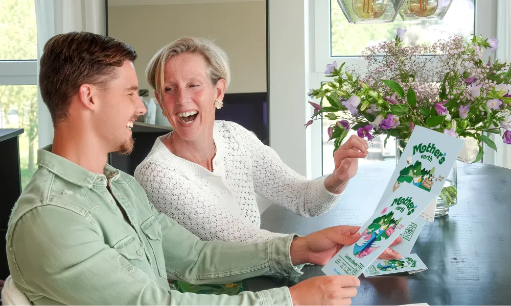 Two people smiling and reading a card at a table with flowers.