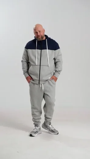 Man in a grey tracksuit stands against a plain background.