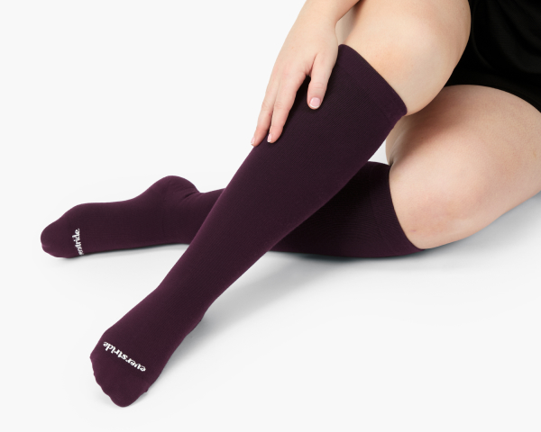 A close-up of a person wearing dark purple, ribbed, knee-high socks against a white background.