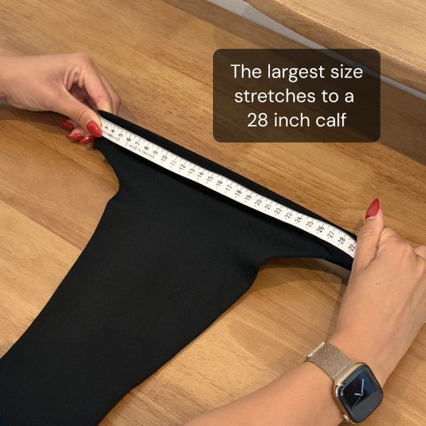 A person's hands stretch a black garment while measuring the top opening with a tape measure.