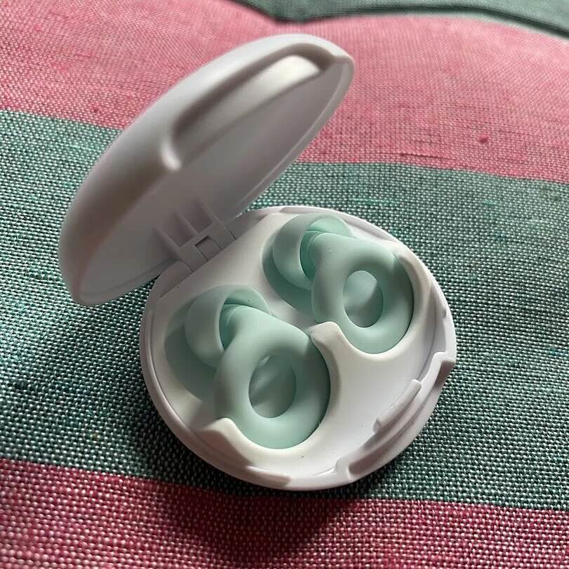 Open white case with mint green earplugs inside on a fabric surface.