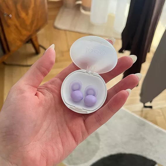 Hand holding a small white case with purple earplugs inside.
