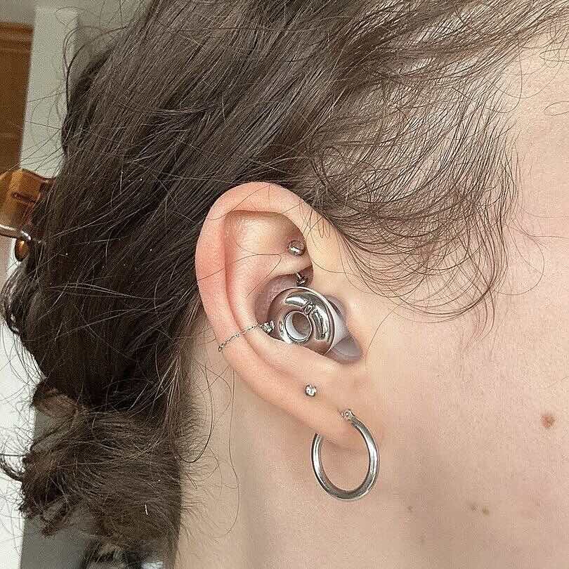 Close-up of an ear with multiple silver piercings, including a large hoop earring.