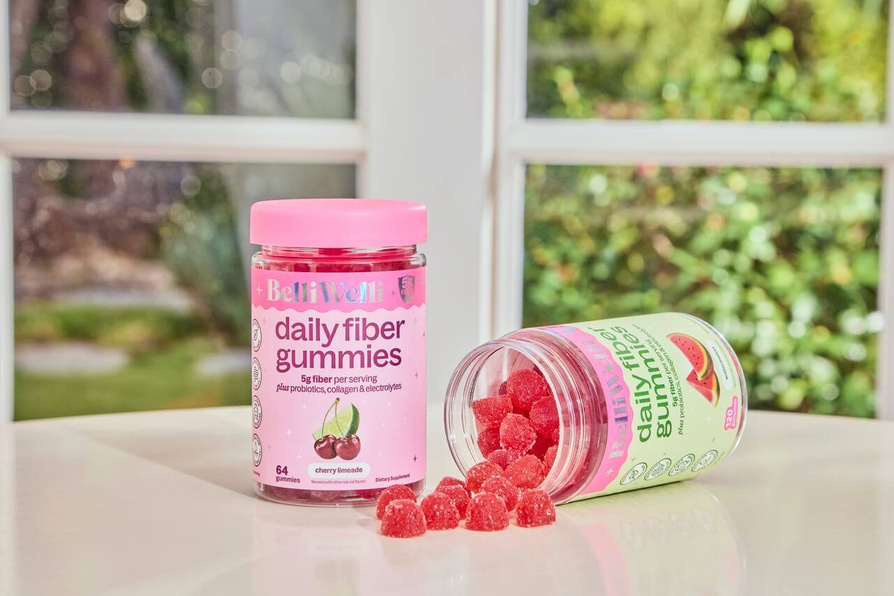 Two bottles of Belli Welli daily fiber gummies on a table, with red gummies spilling from one.