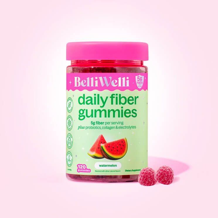 A bottle of BelliWelli watermelon-flavored daily fiber gummies with two gummies beside it on a pink background.