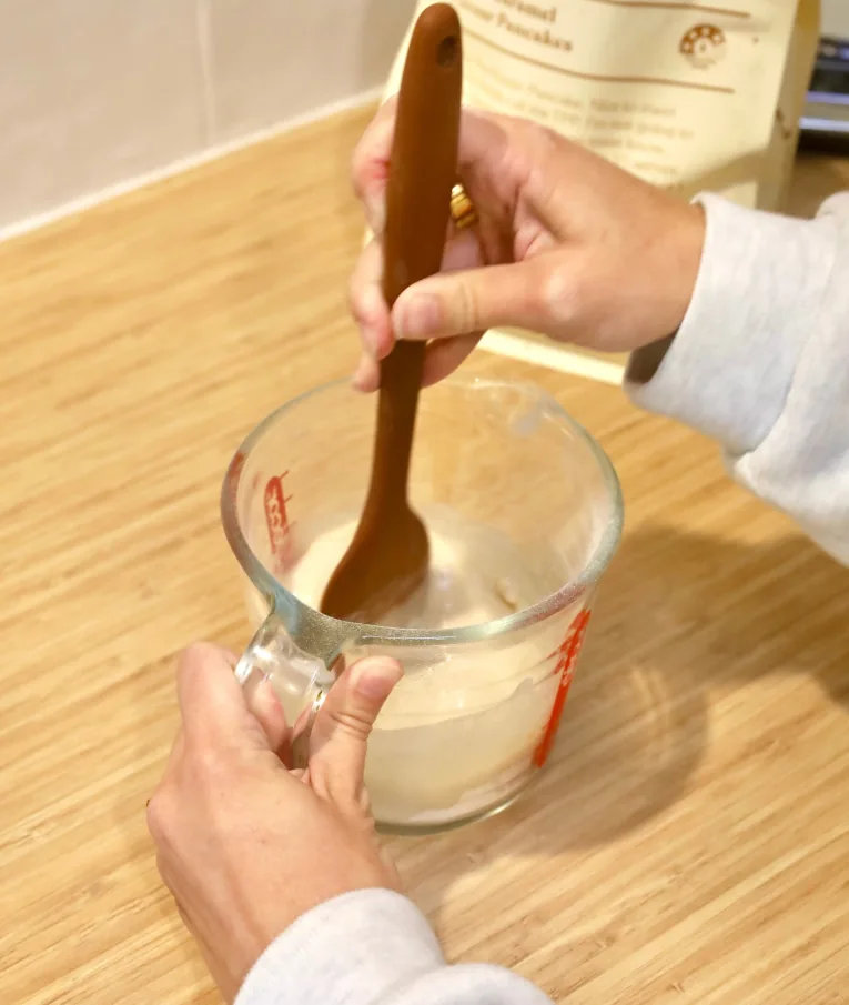 Person stirring batter in a measuring cup on a wooden surface.
