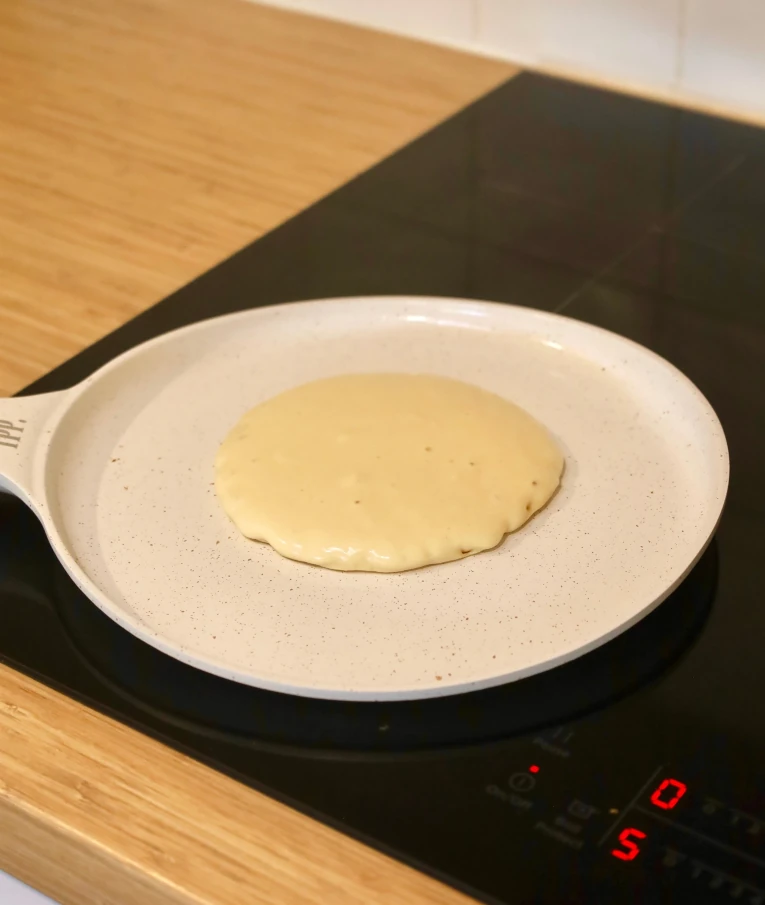 A pancake cooking on a stovetop in a white pan.