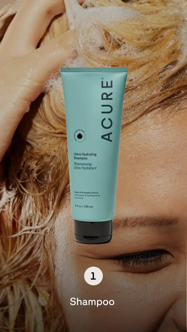 Person washing their blonde hair with blue product bottle in the foreground. Step 1 shampoo.