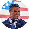 Man in suit speaking at a podium with an American flag in the background.
