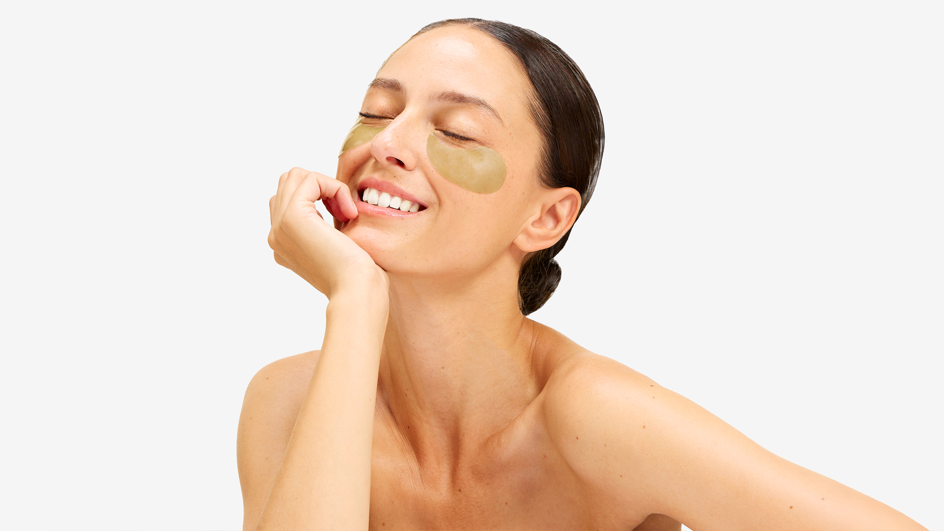 Person smiling with under-eye patches and closed eyes.