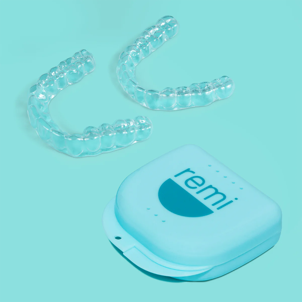 Two clear dental aligners and a blue case on a turquoise background.