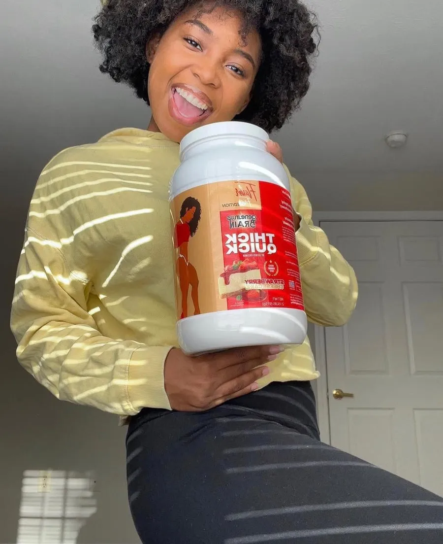 A smiling woman in a yellow sweatshirt holds up a large tub of protein powder.
