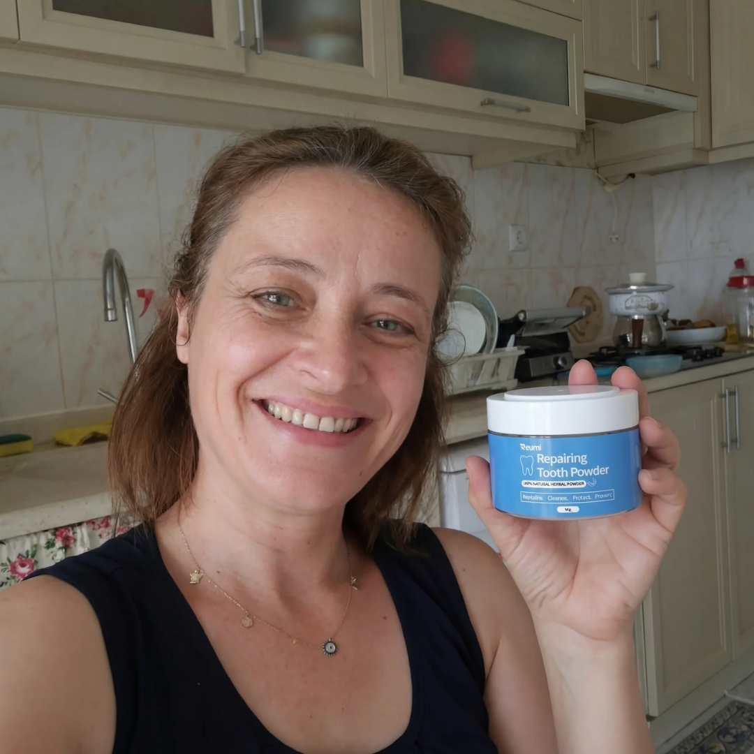 A smiling woman in a kitchen holds up a blue and white container of Repairing Tooth Powder.