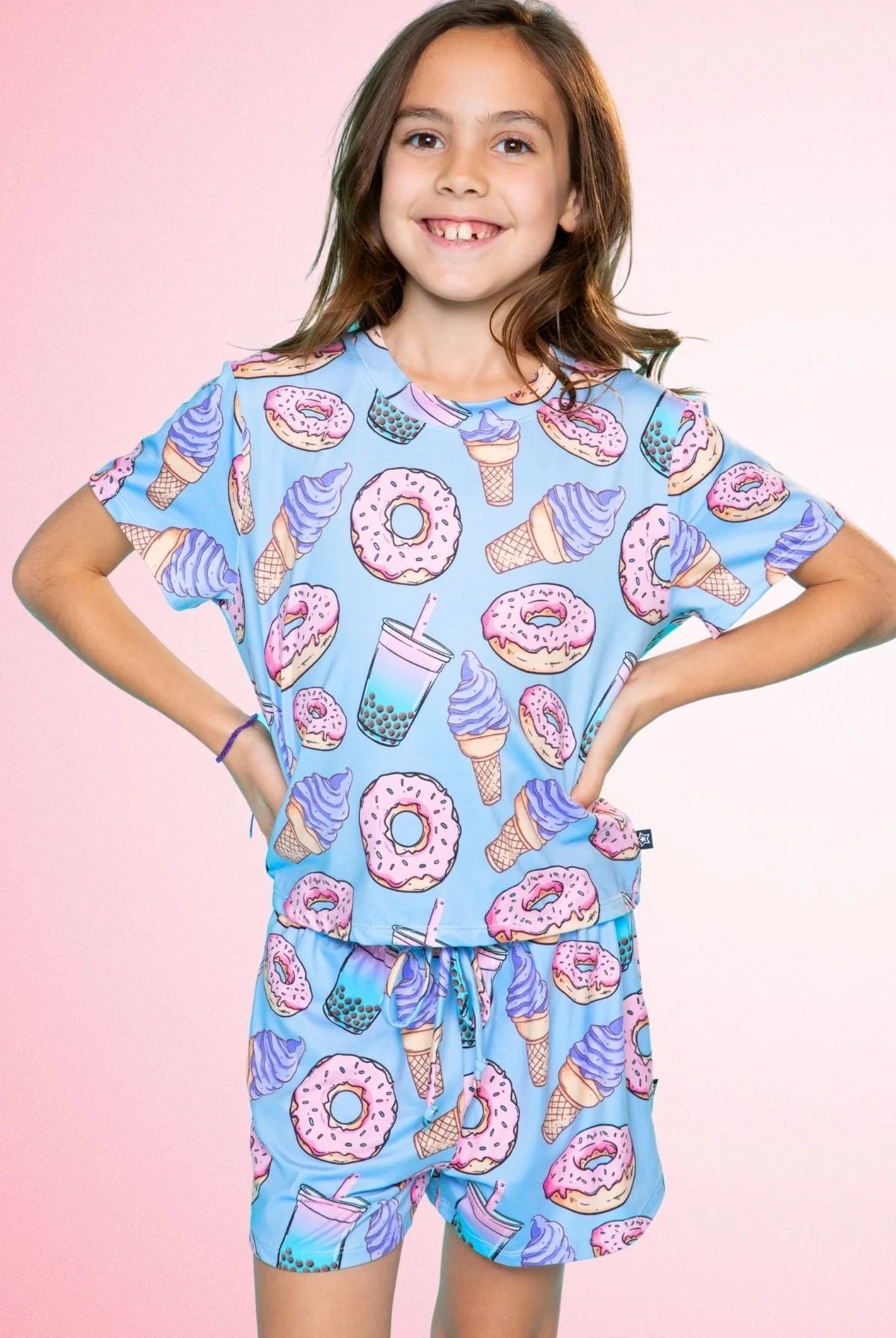 Child wearing a blue outfit with donut and ice cream print, smiling against a pink background.