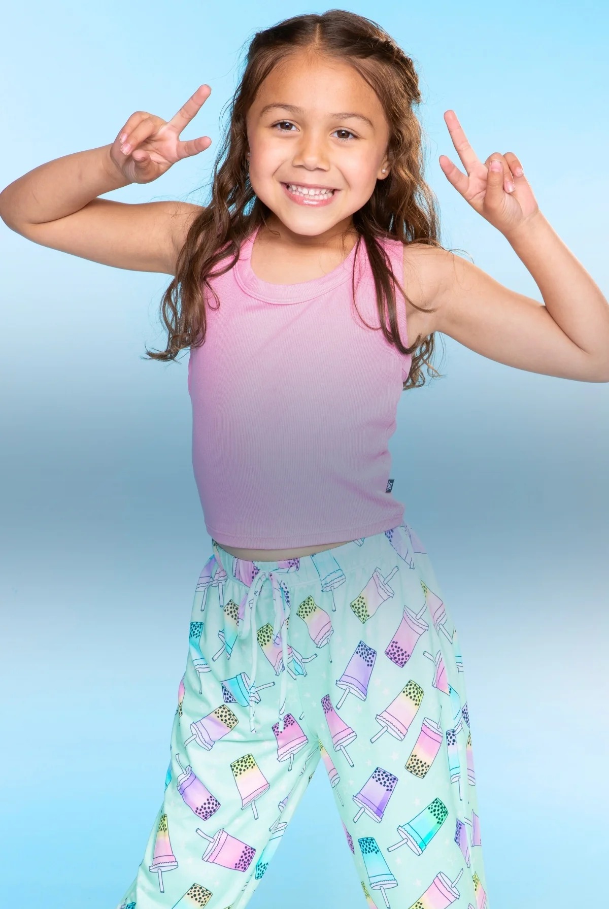 Smiling child in pink top and patterned pants, making peace signs.