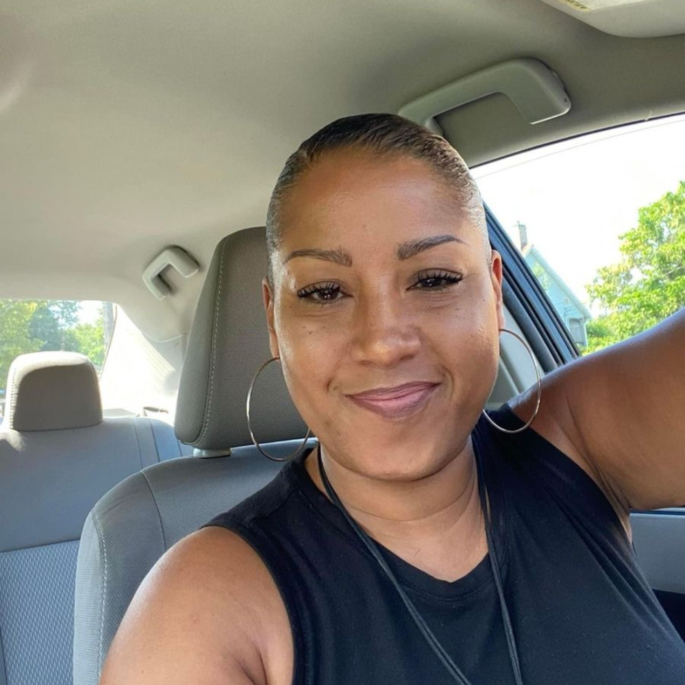 Person smiling inside a car, wearing a black top.