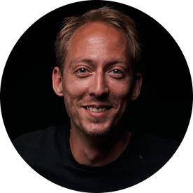 Smiling man with short hair against a dark background.
