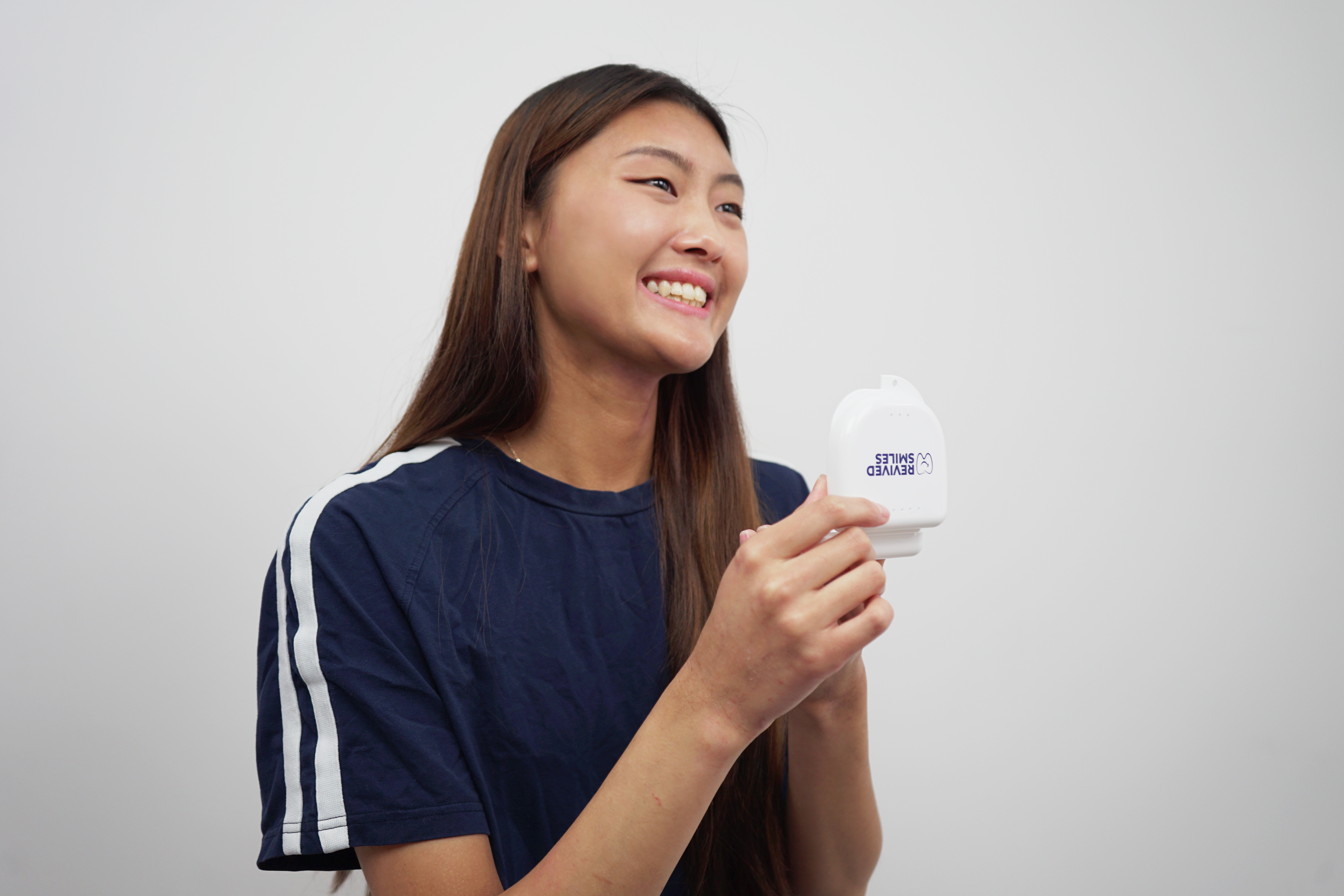 Person smiling, holding a small white device with text.