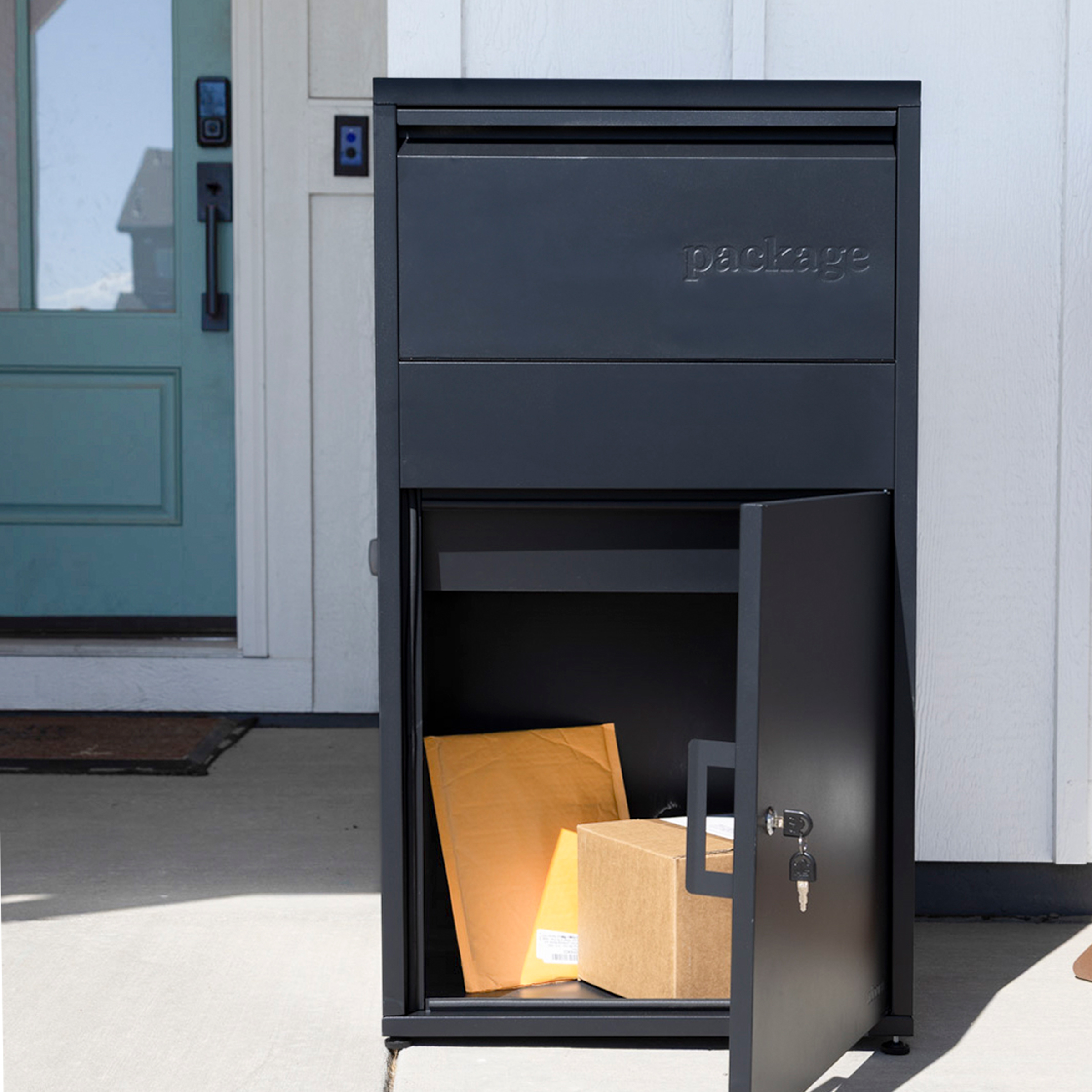 Black package drop box with open door, containing parcels, near a teal door.