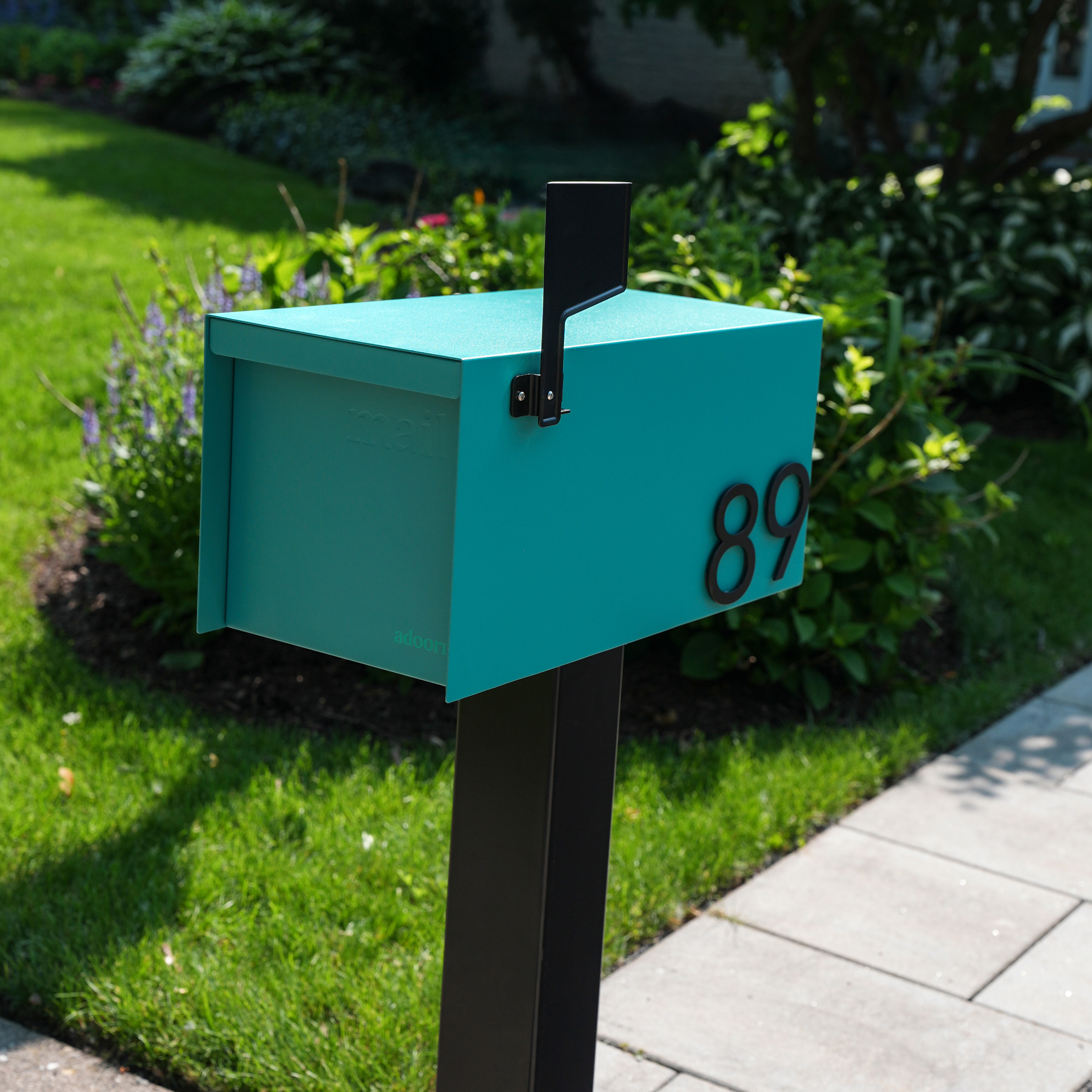 A teal mailbox with the number 89 in a garden setting.