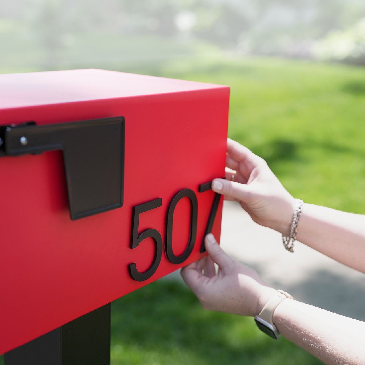 Person attaching numbers to a red mailbox outdoors.