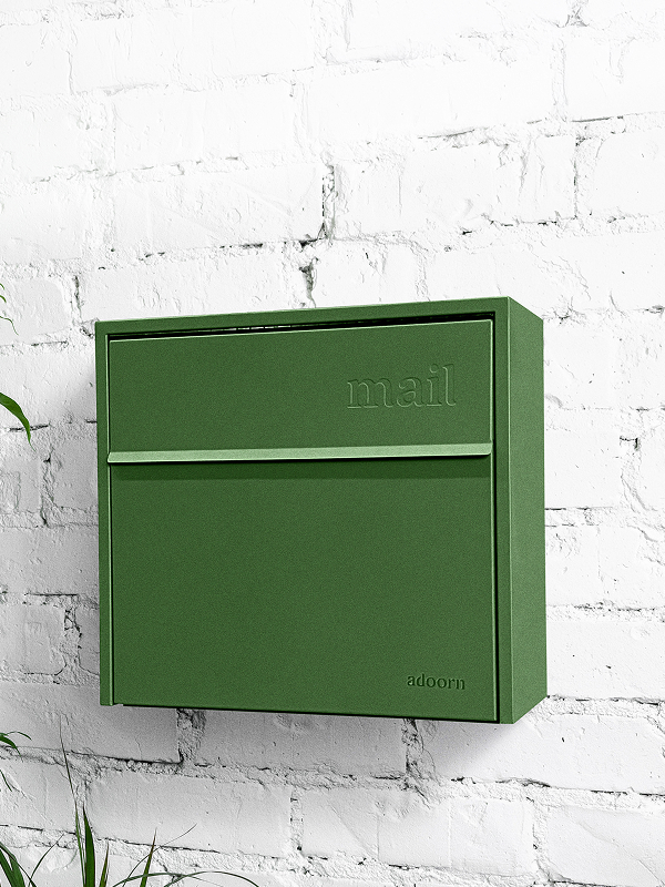 Green wall-mounted mailbox on a white brick wall.
