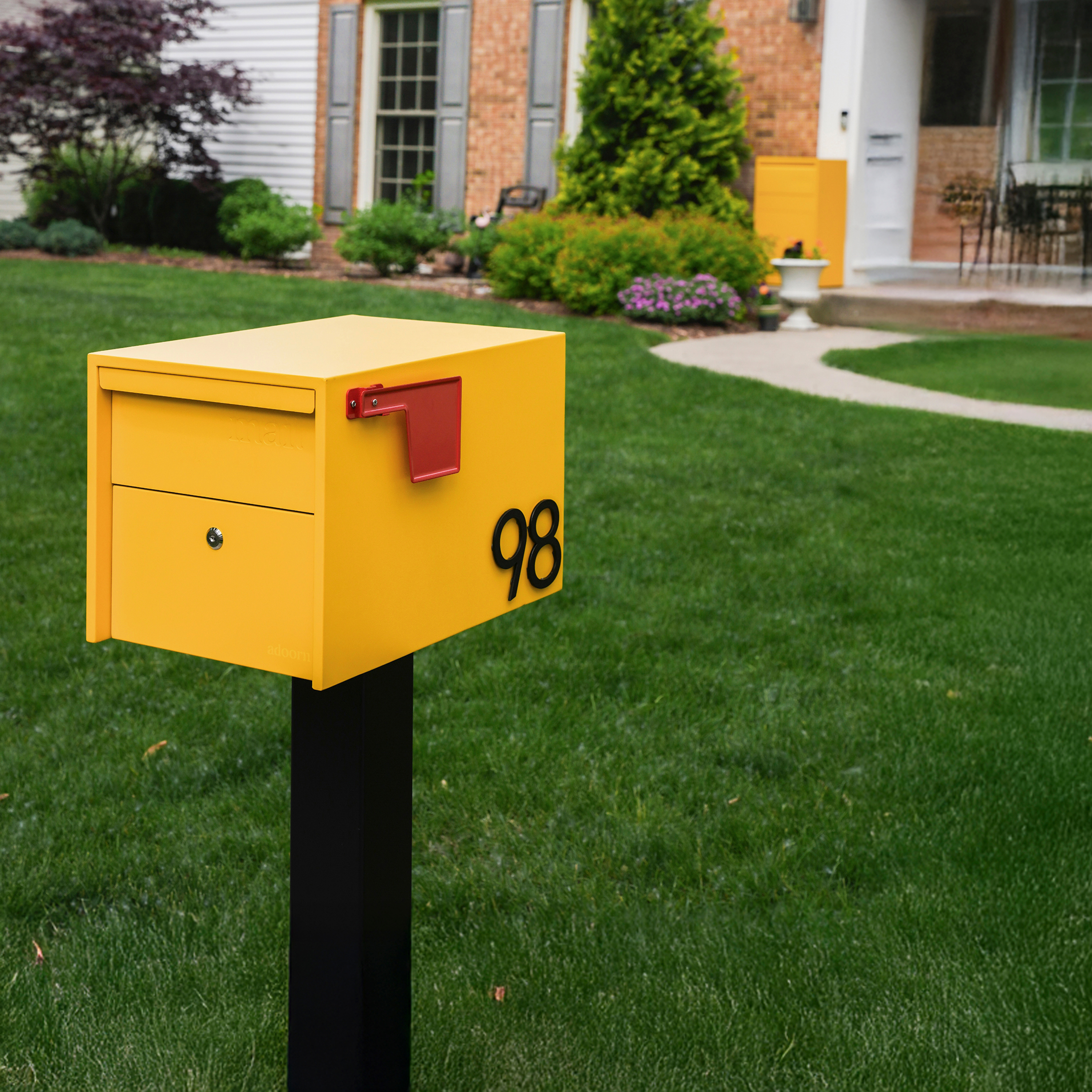 Yellow mailbox with number 98 on a lawn in front of a house.
