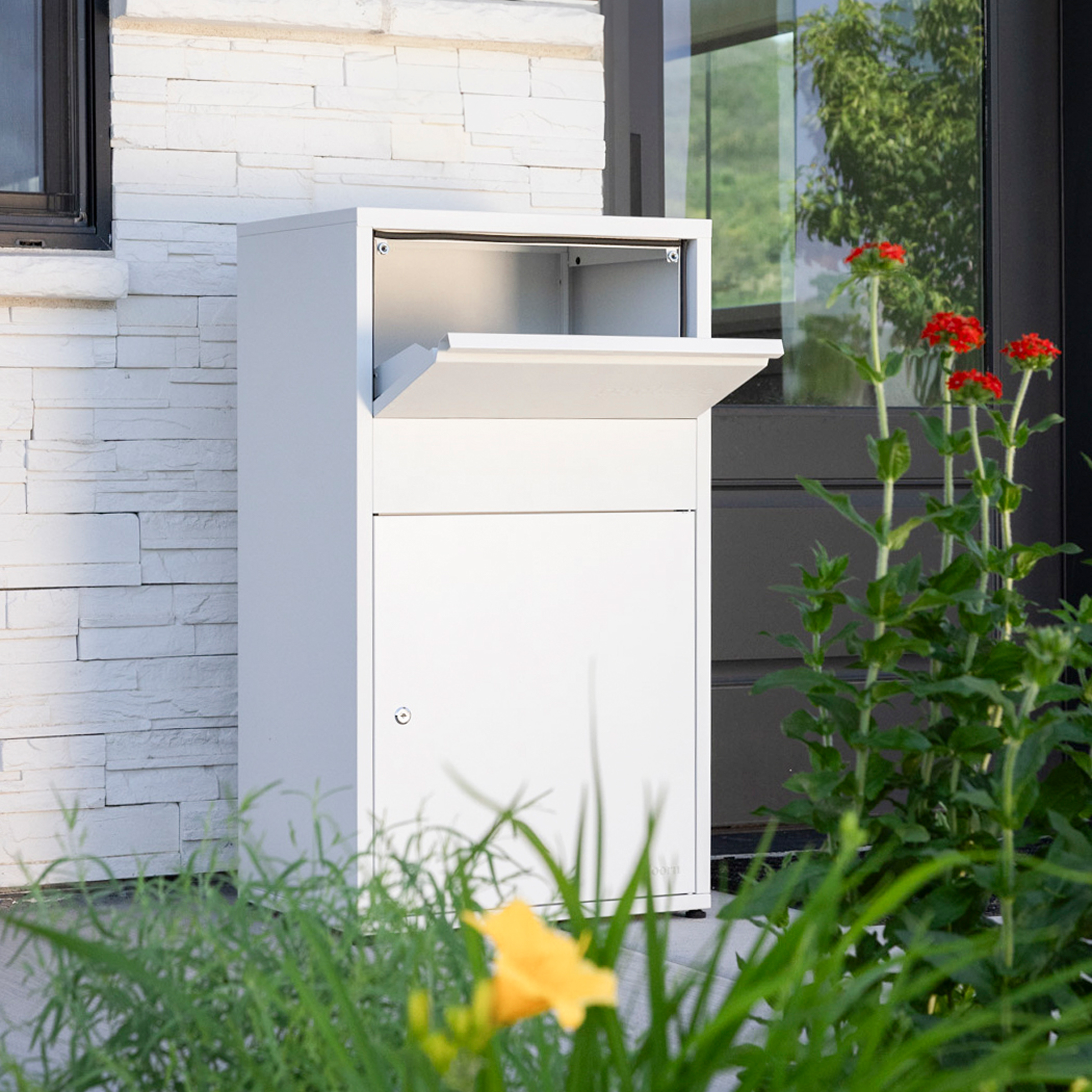White parcel drop box near a house entrance with flowers in the foreground.
