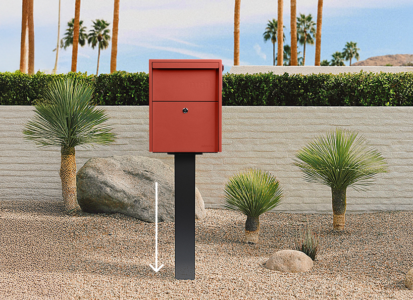 Red mailbox on a black post in a desert garden with palm trees.