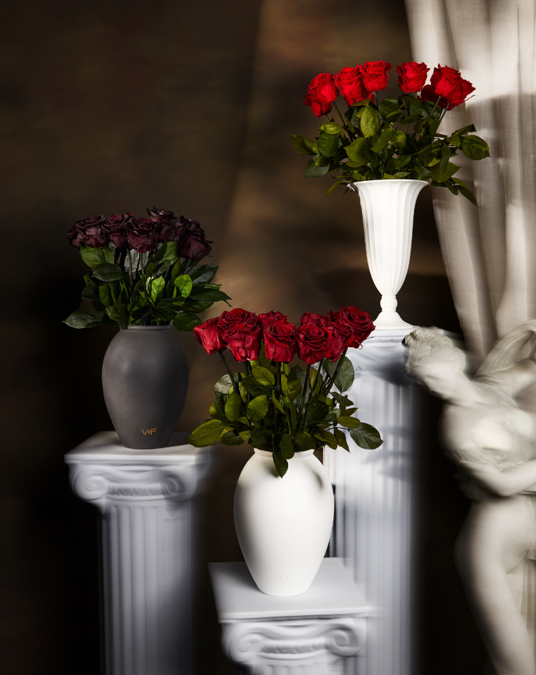 Three vases with red and dark red roses on white pedestals.