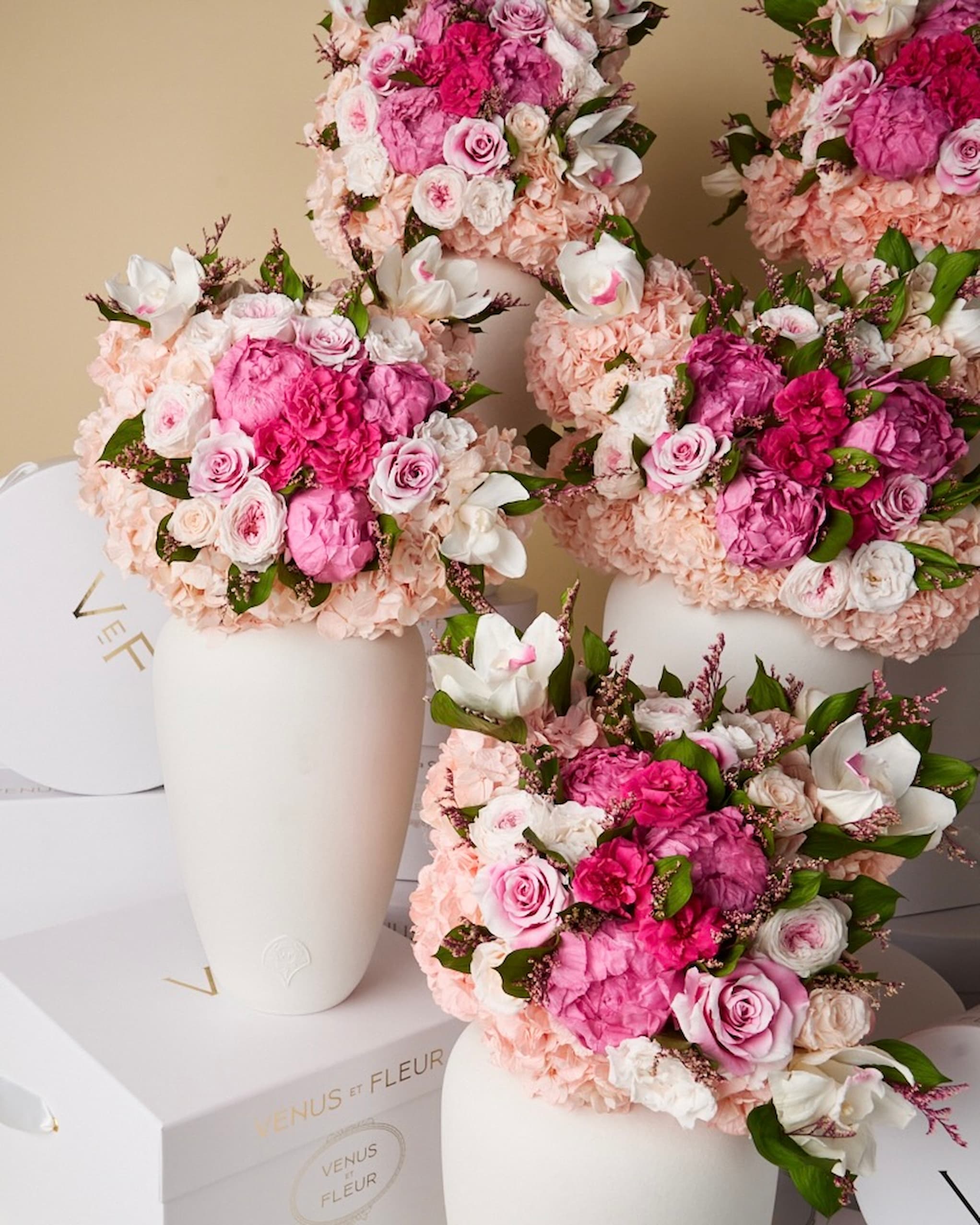 Several large, lush arrangements of pink, fuchsia, and white flowers in matte white vases.