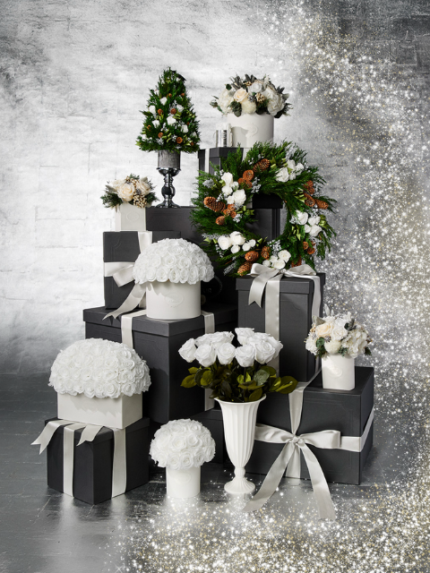 Stacked black boxes with white bows, floral arrangements, and a Christmas tree.
