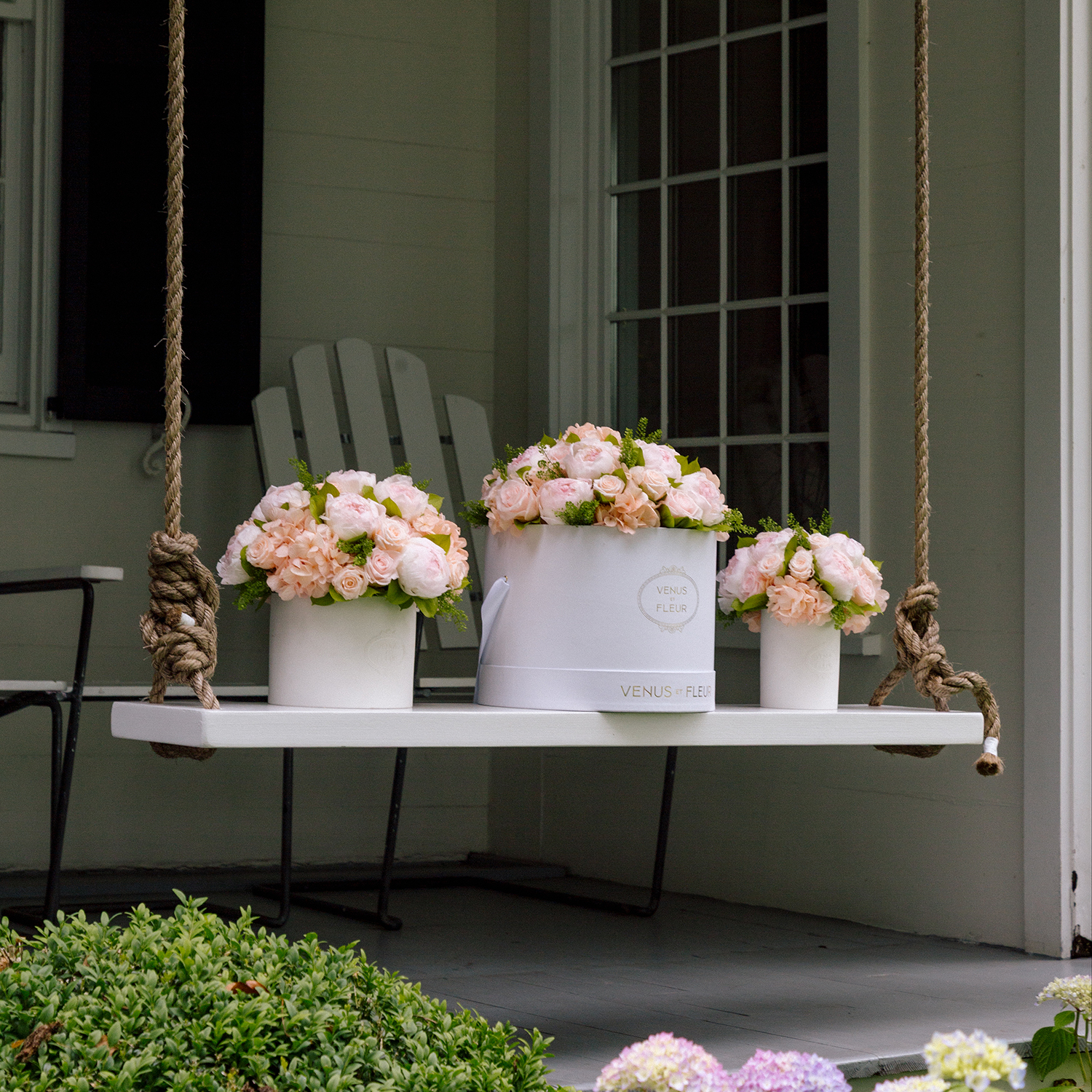 White swing with pink flower arrangements in white boxes on a porch.