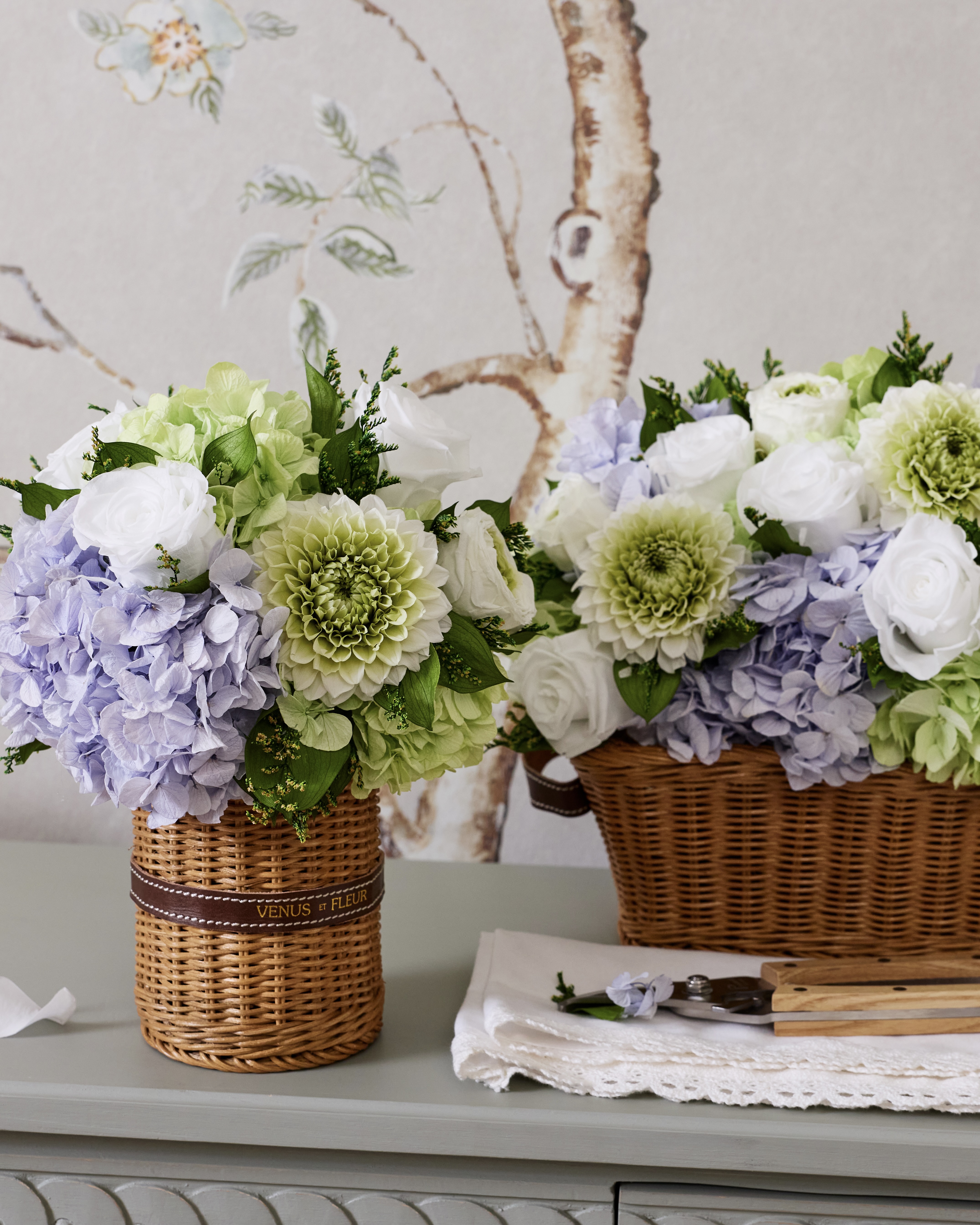 Two wicker baskets filled with purple, green, and white flowers sitting on a grey table.
