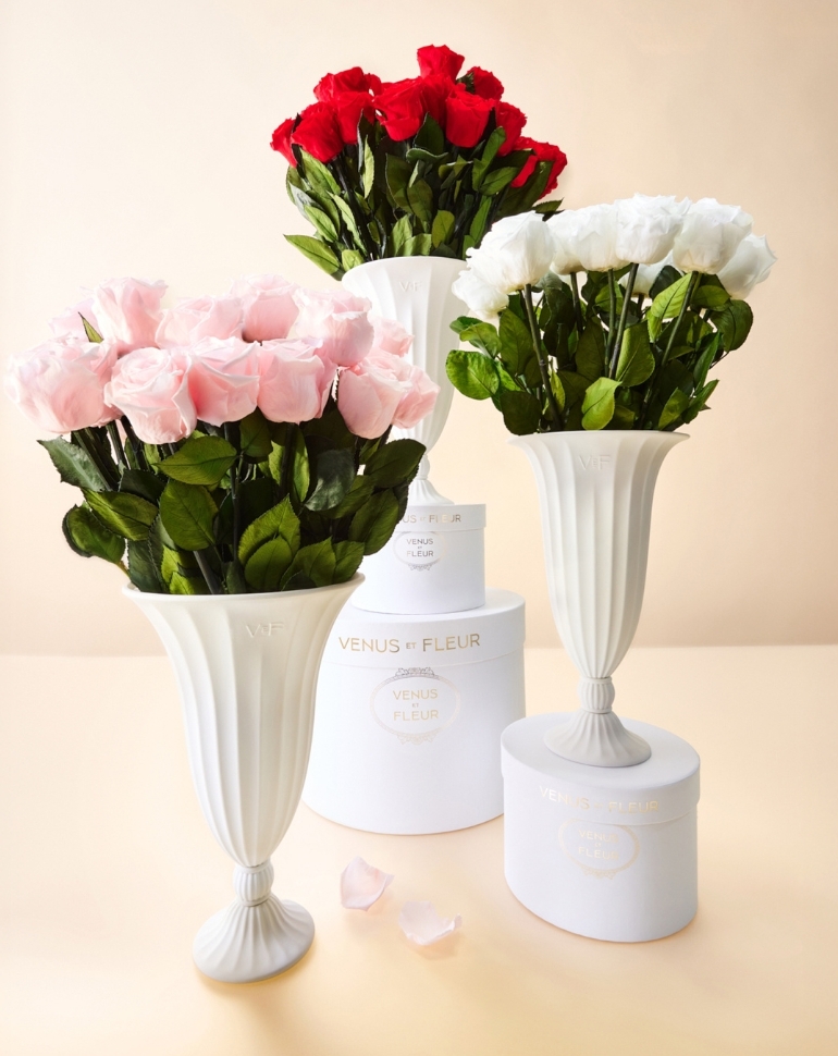 Three white vases filled with pink, red, and white roses sit with matching round gift boxes.