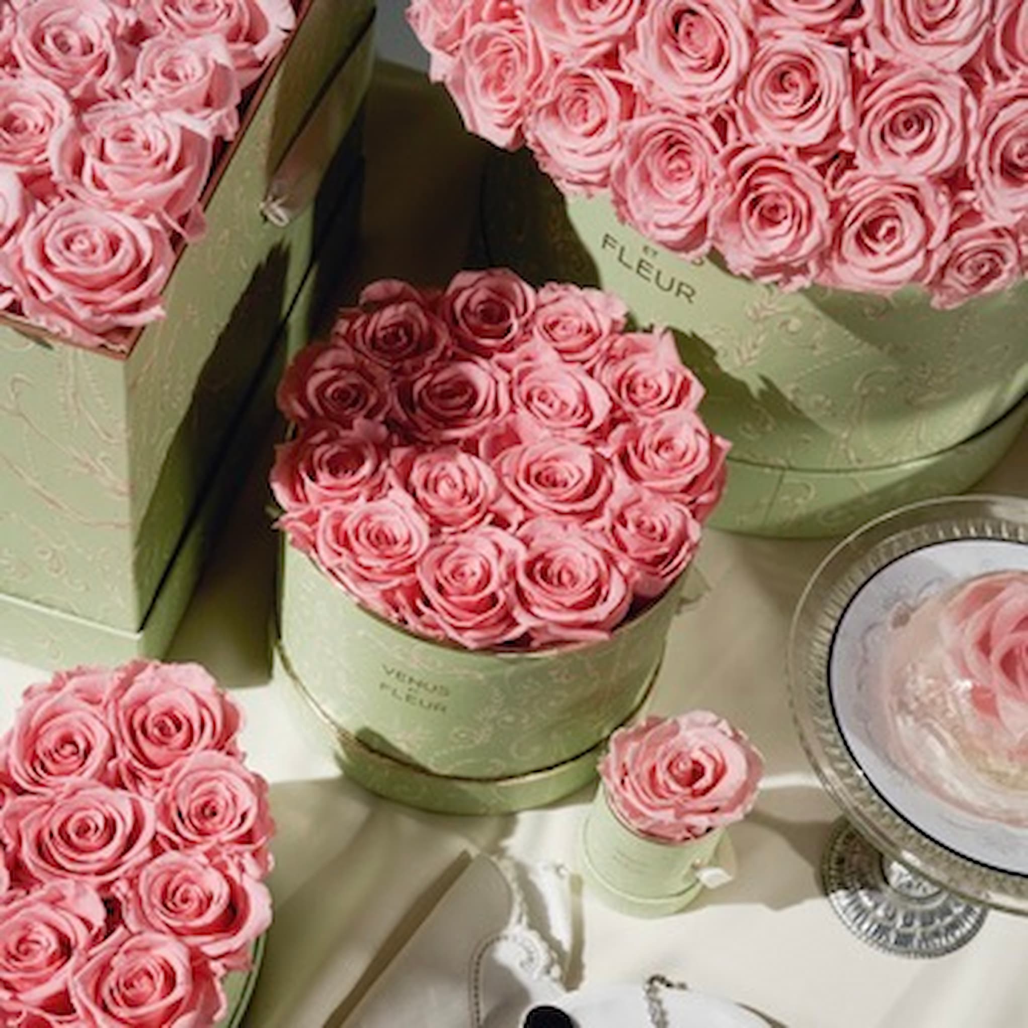 An assortment of pink roses in various sizes of light green, decorative boxes.