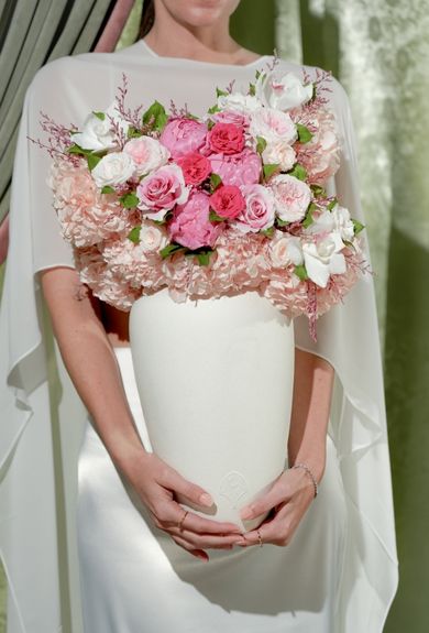 Person holding a white vase with pink and white flowers.